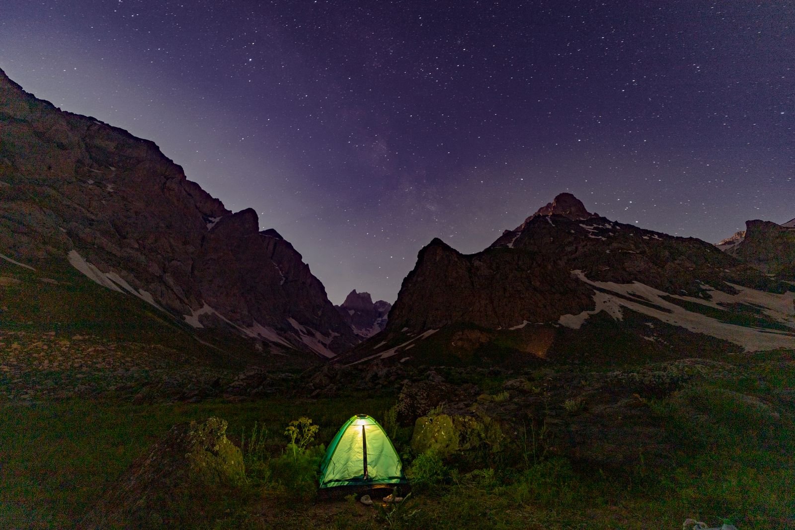 Glowing tent under a starry sky at a mountain campsite