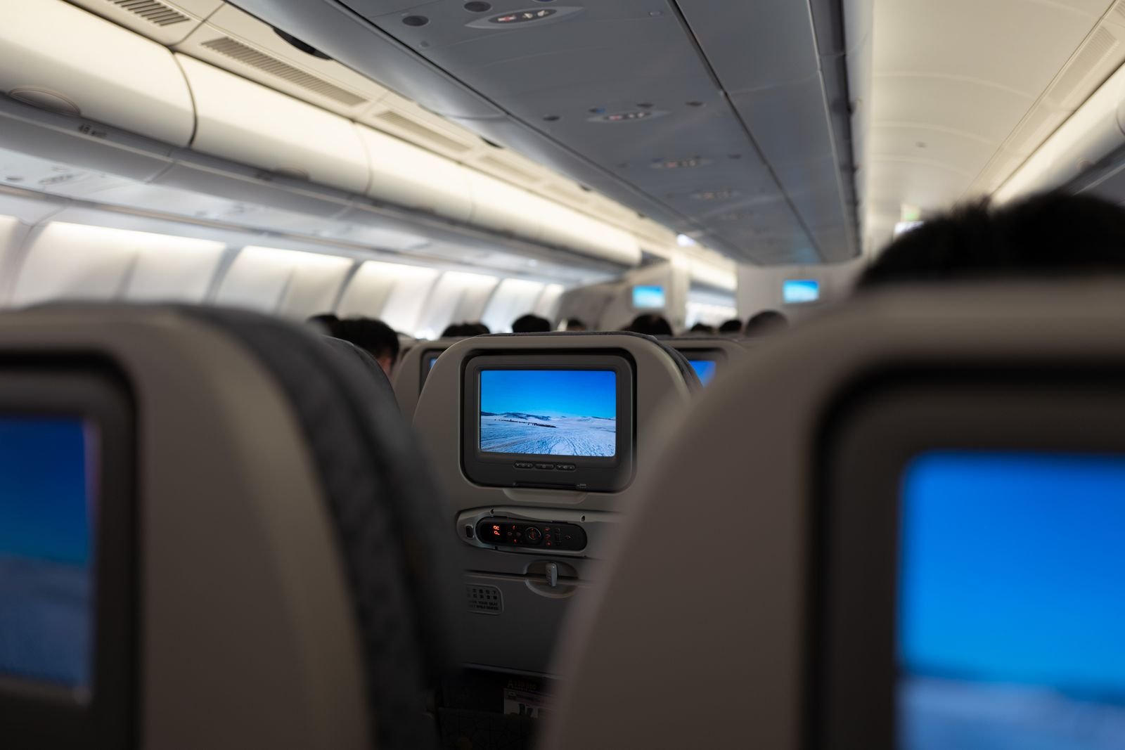 Airliner cabin with seatback screens — the flight both booking routes sell