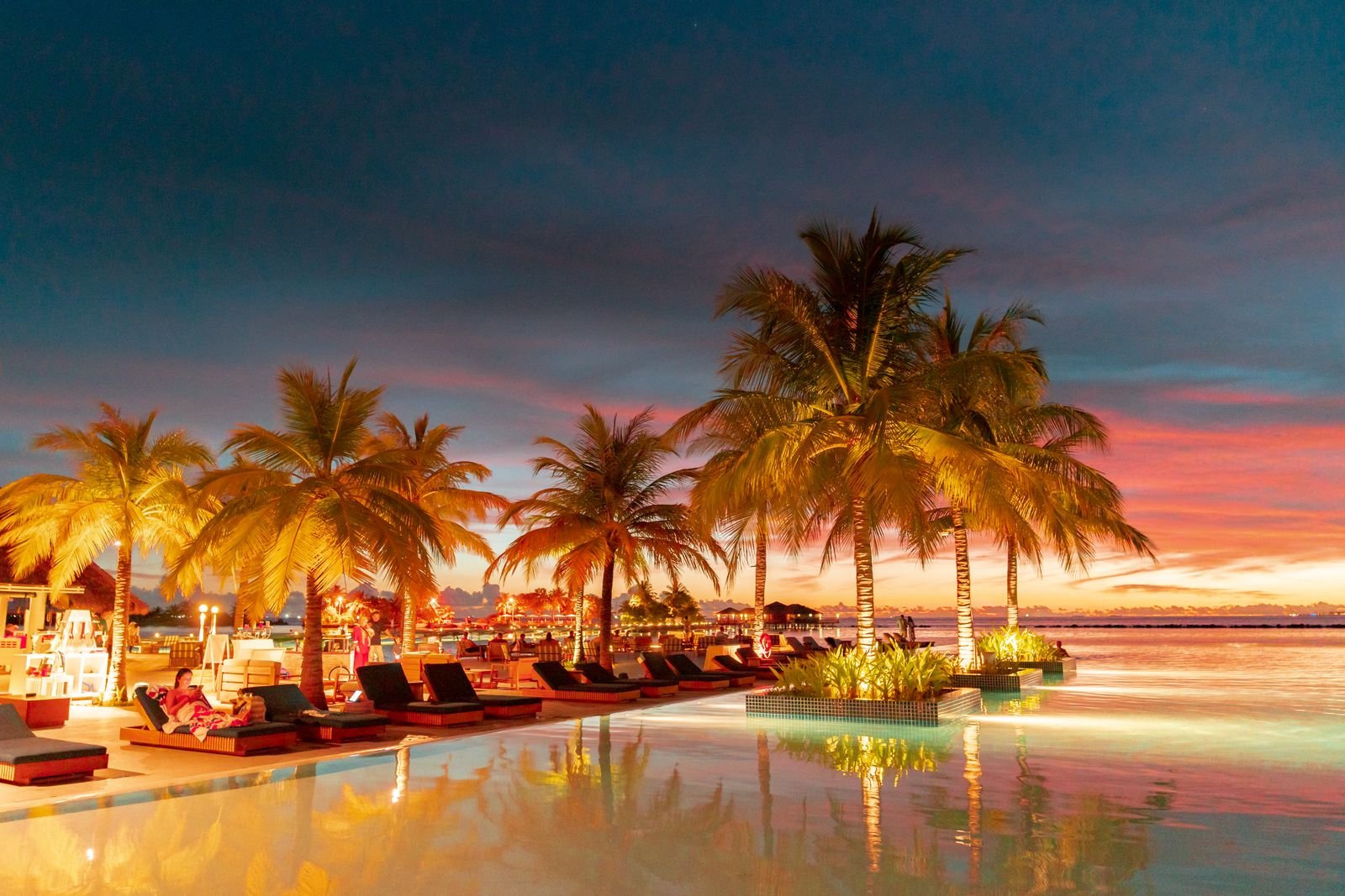 Guests relaxing in an infinity pool at a seaside resort at sunset